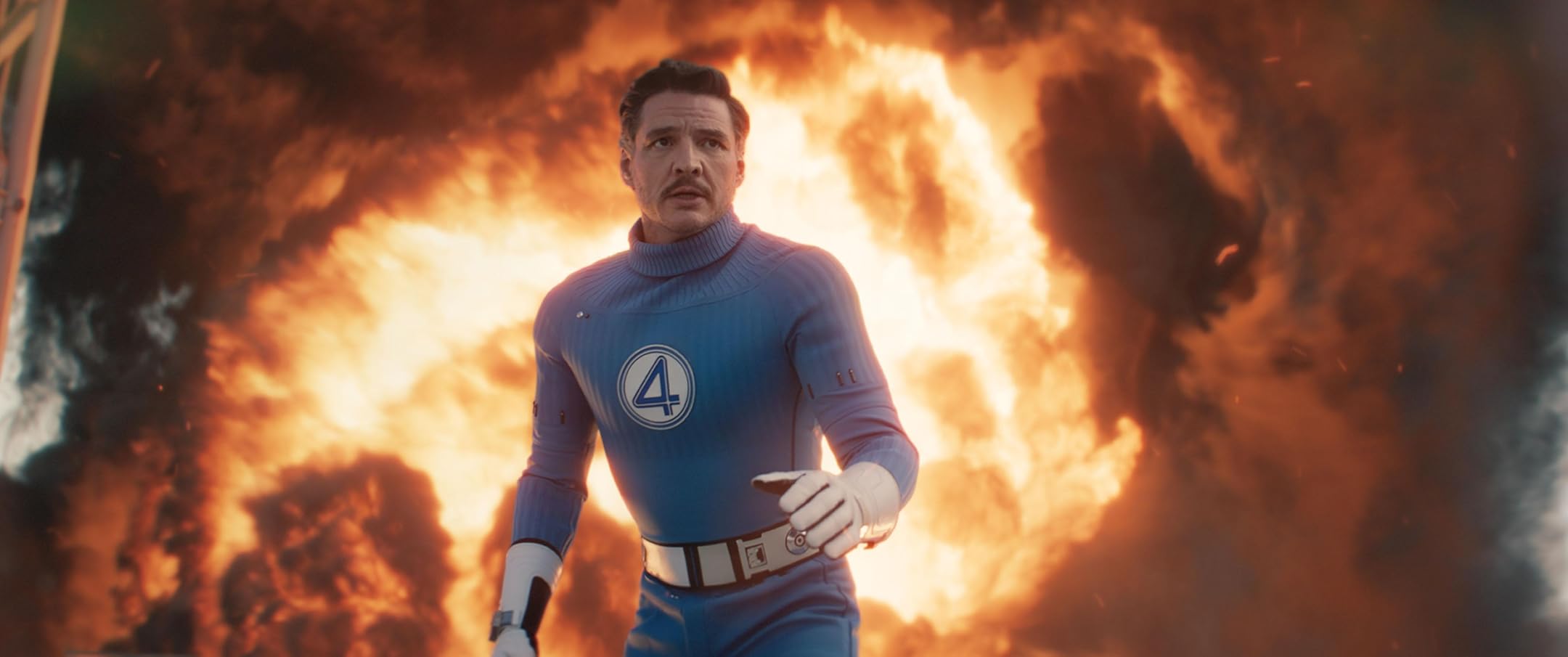 Reed Richards (Pedro Pascal) stands in front of a massive explosion in a still from The Fantastic Four: First Steps.